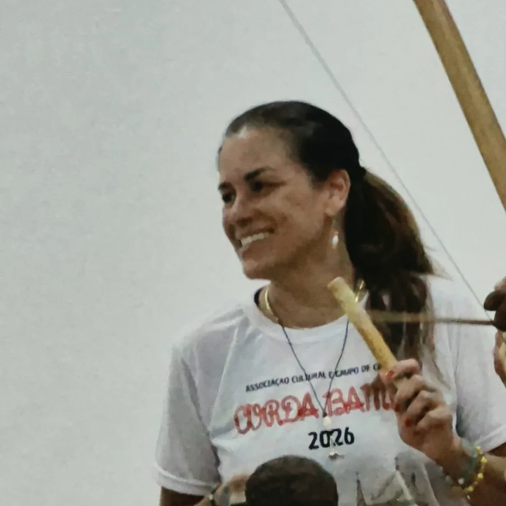 Sarita Del Sol sorrindo e tocando um instrumento em uma roda de capoeira